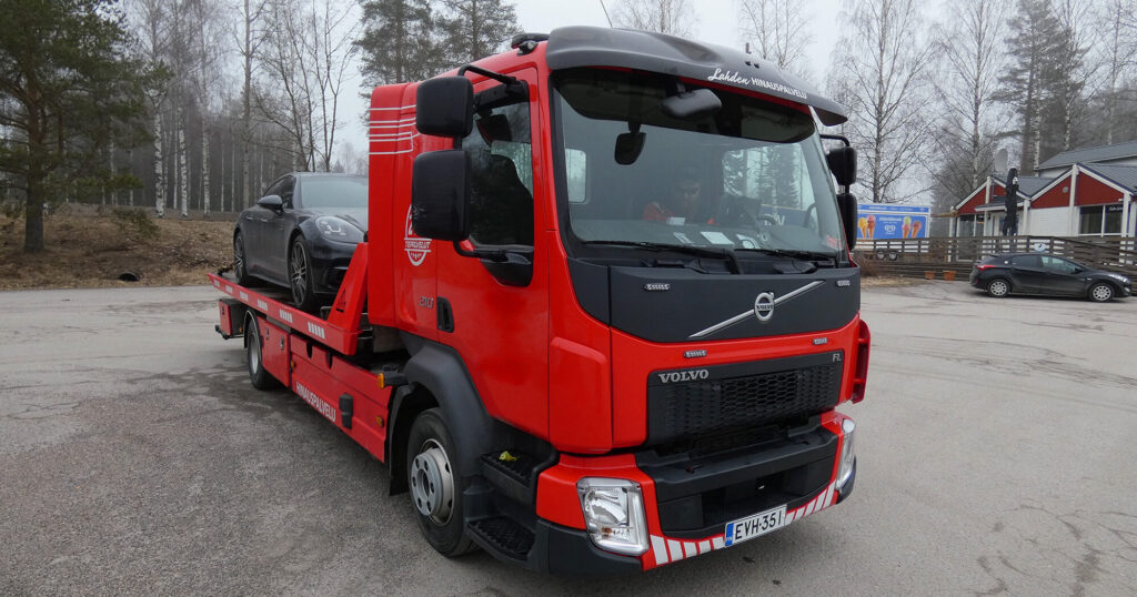 Punainen hinausauto kuljettaa mustaa henkilöautoa